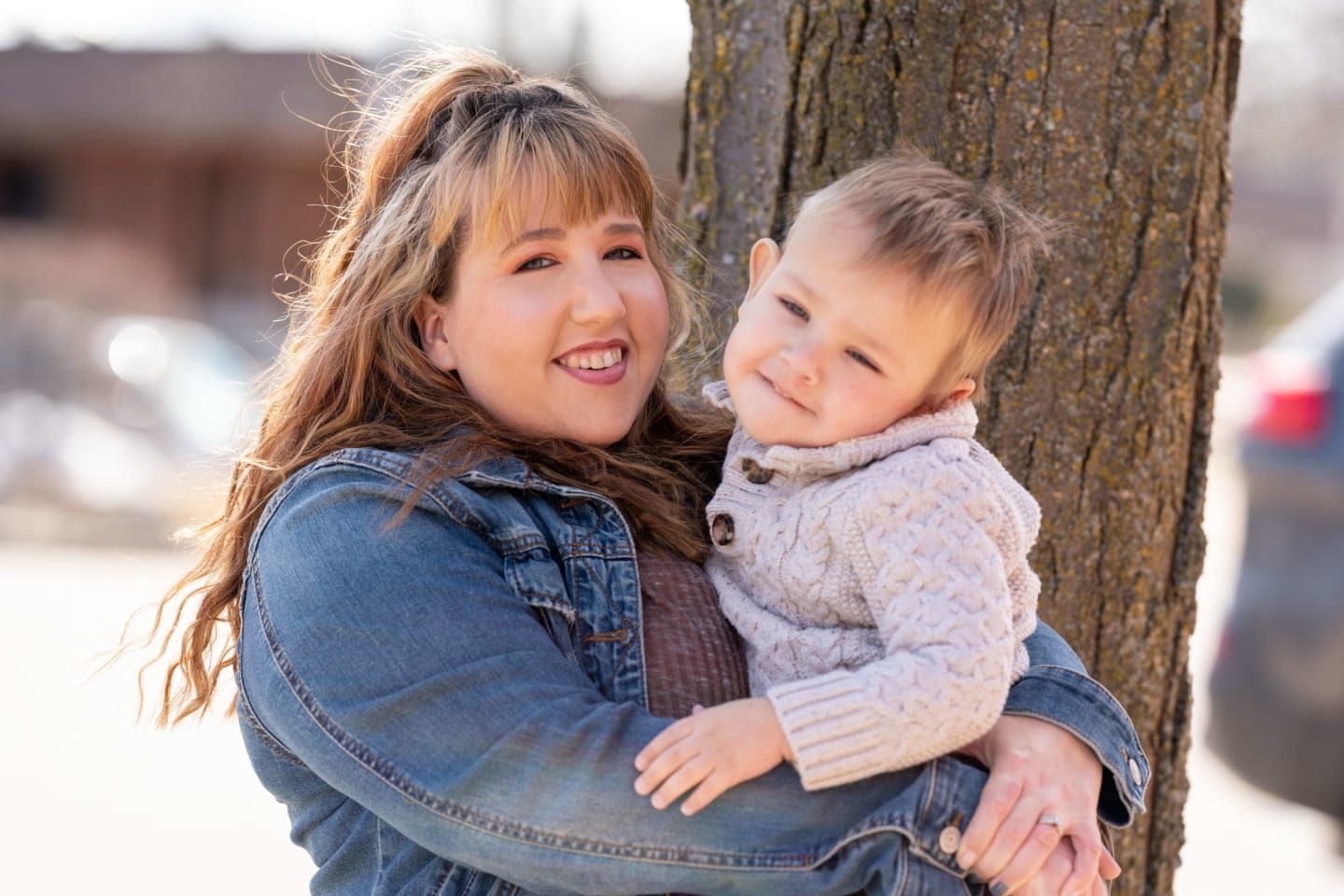 Kym Pfister holding her 2-year-old-son, Gus, in front of a tree trunk