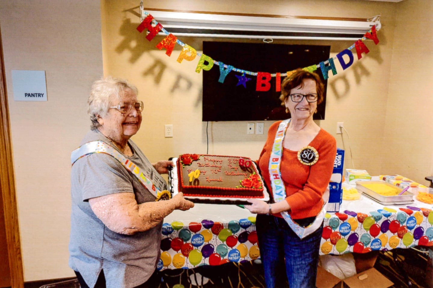 Laurel and her sister, Peg smiling and holding a birthday cake together.