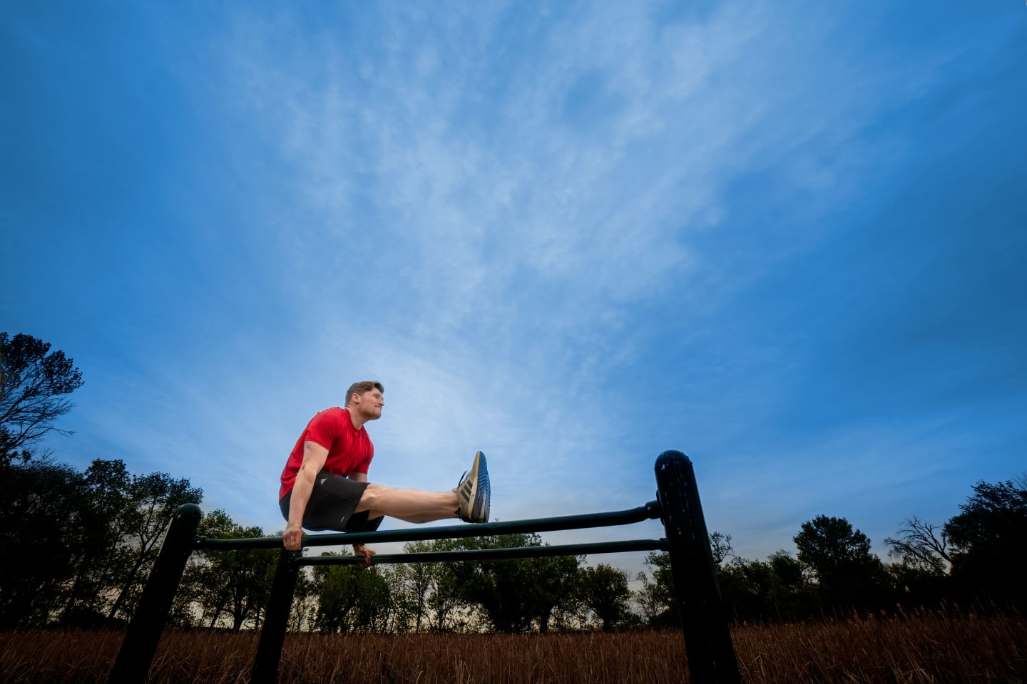 Casey McDermott doing strength exercises on a set of outdoor parallel bars