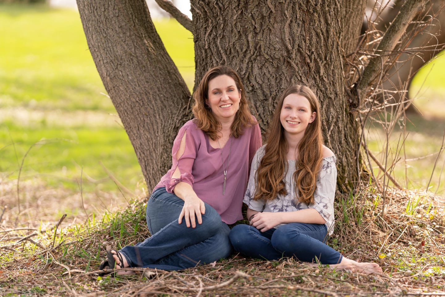 Annika Wyant and her mother, Janna, sitting in grass in front of a tree trunk