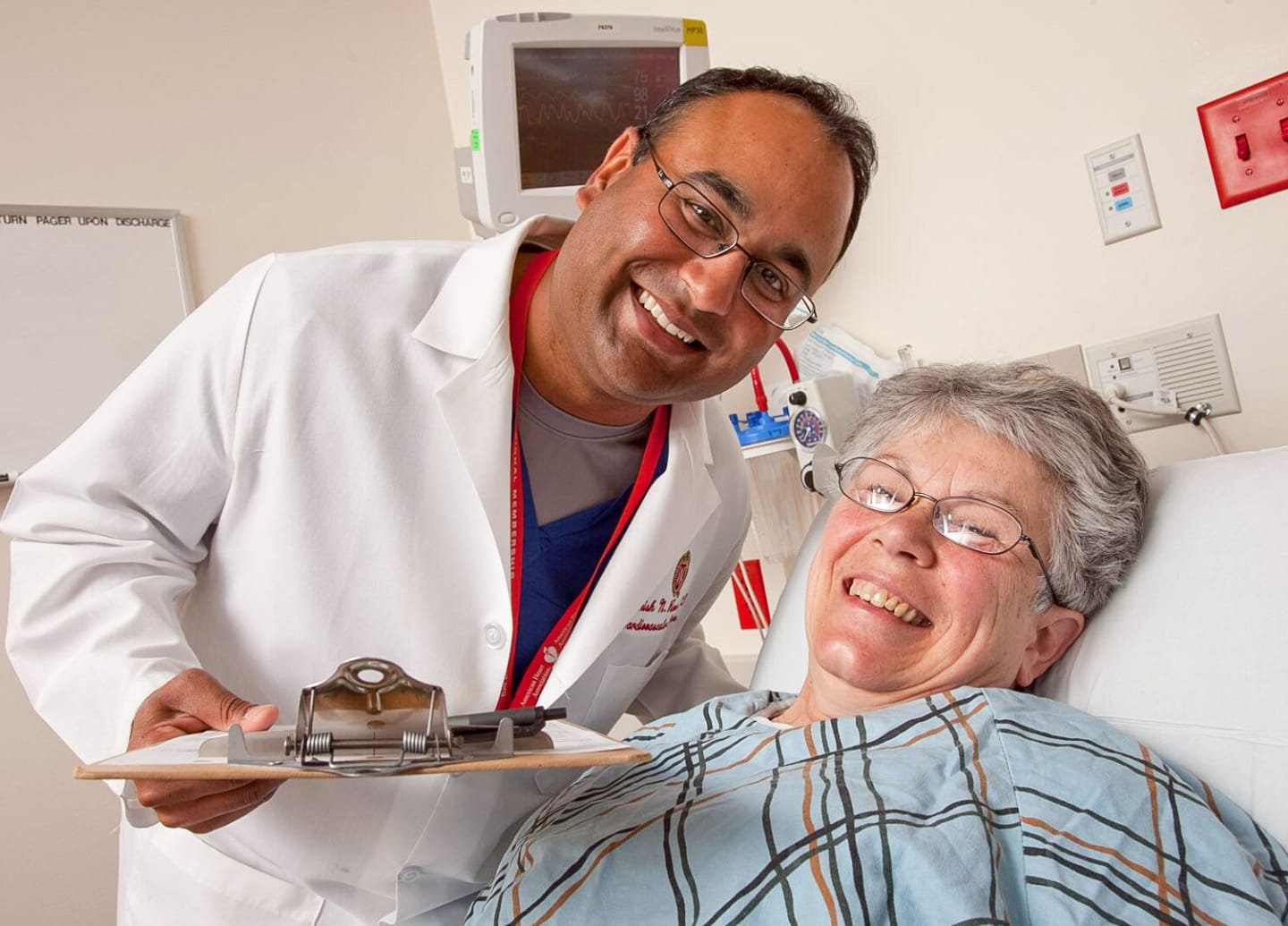 A physician leaning over a smiling patient in a hospital bed