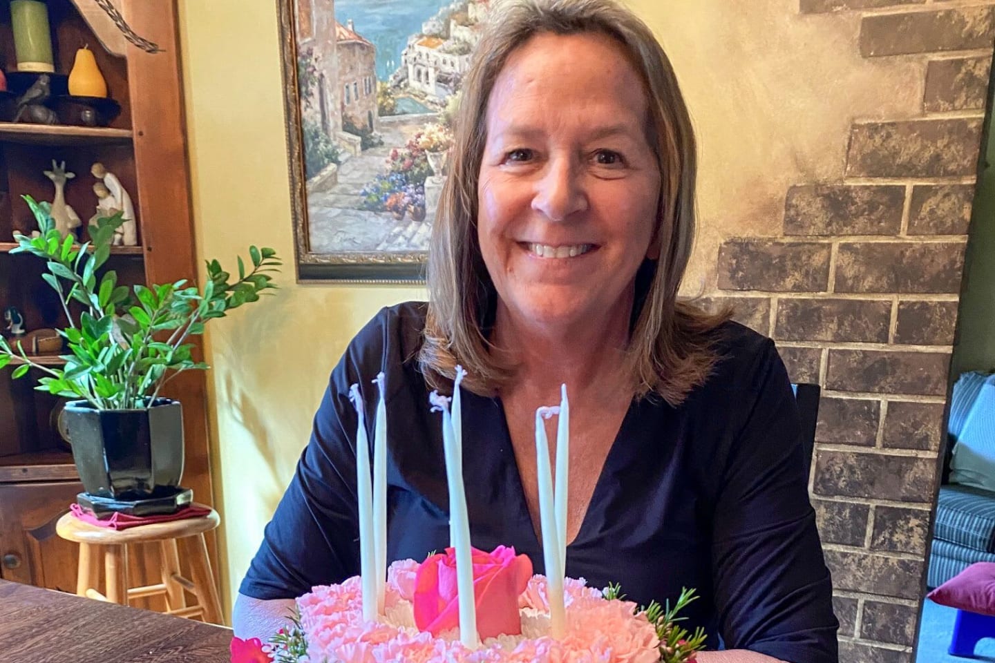 Becky, smiling behind a birthday cake decorated with pink flowers.