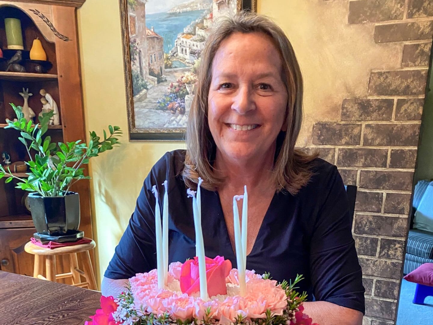 Becky, smiling behind a birthday cake decorated with pink flowers.