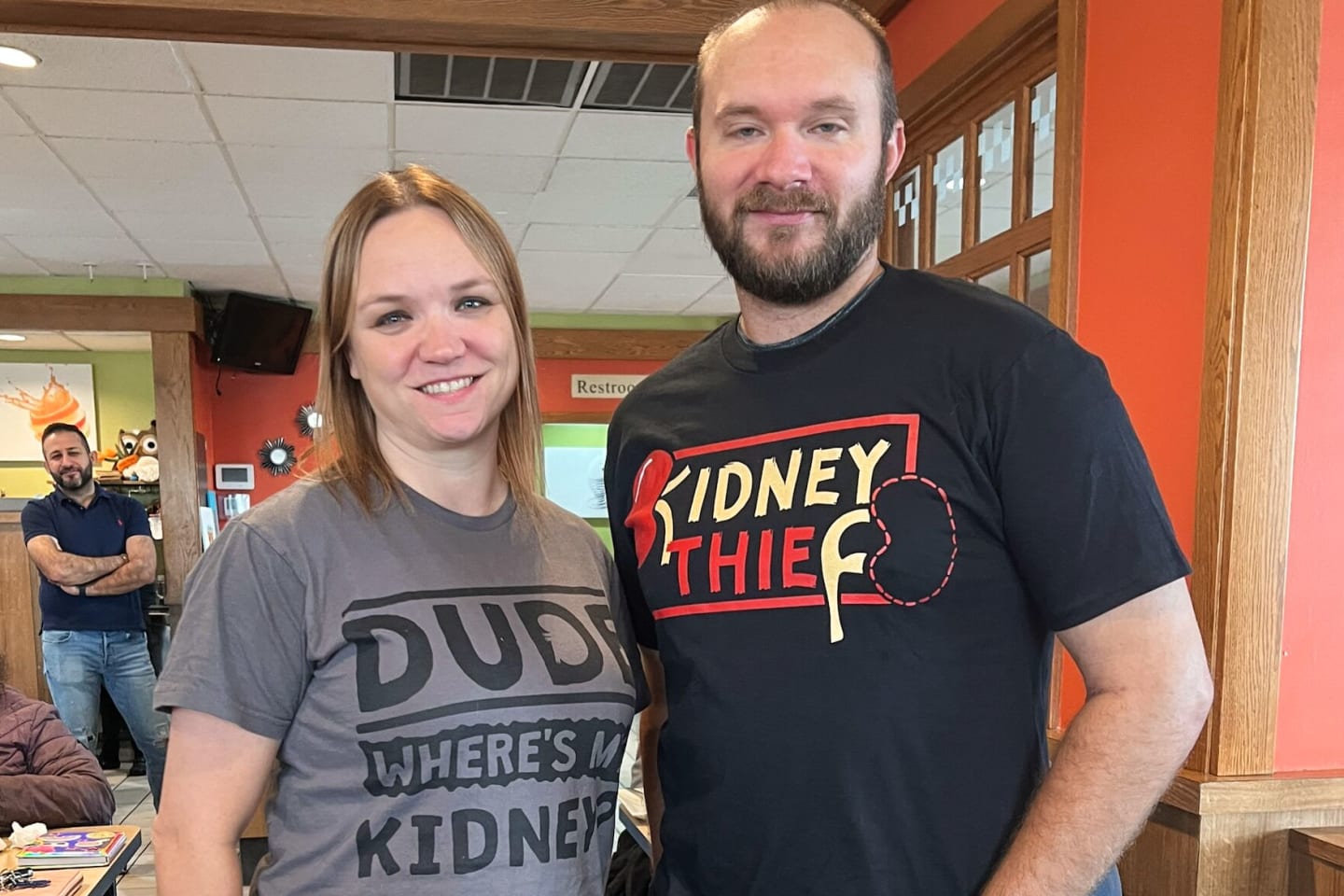 Woman wearing a shirt that says, "Dude, where's my kidney?" standing next to man wearing a shirt that says, "Kidney thief."