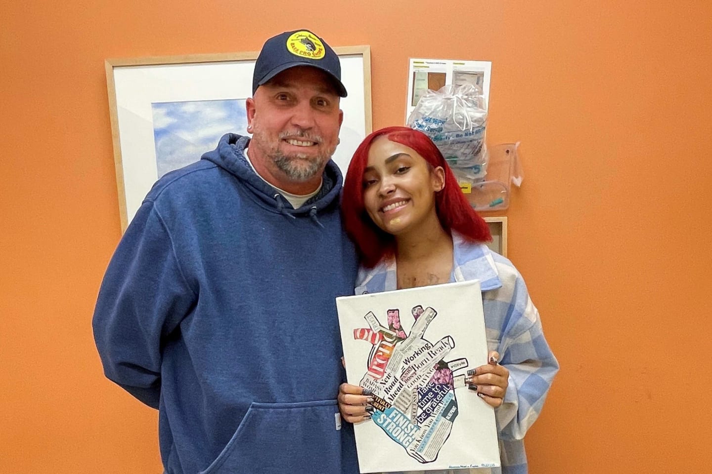 A girl, smiling next her dad, holding a picture of a heart.