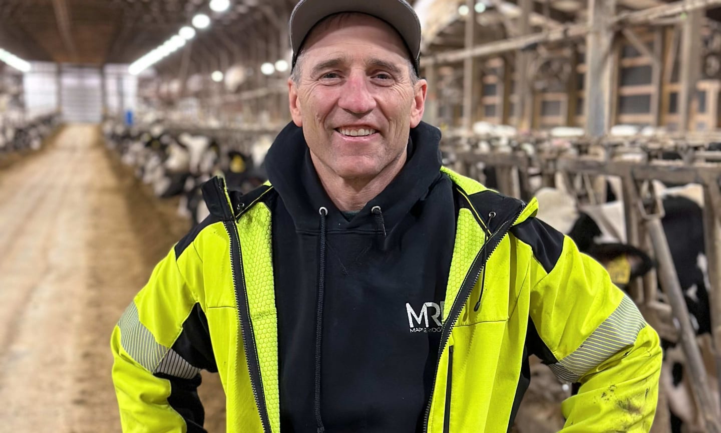 Man in yellow jacket, smiling inside of cow barn.