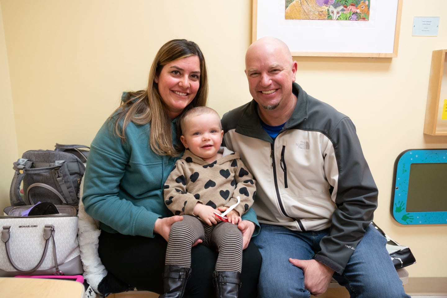 Kinsley Judd sitting with her parents, Sarah and Ryan, inside a hospital room