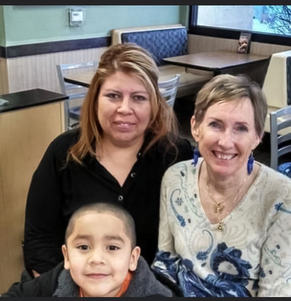 A small boy posed in front of two adult women, all smiling.