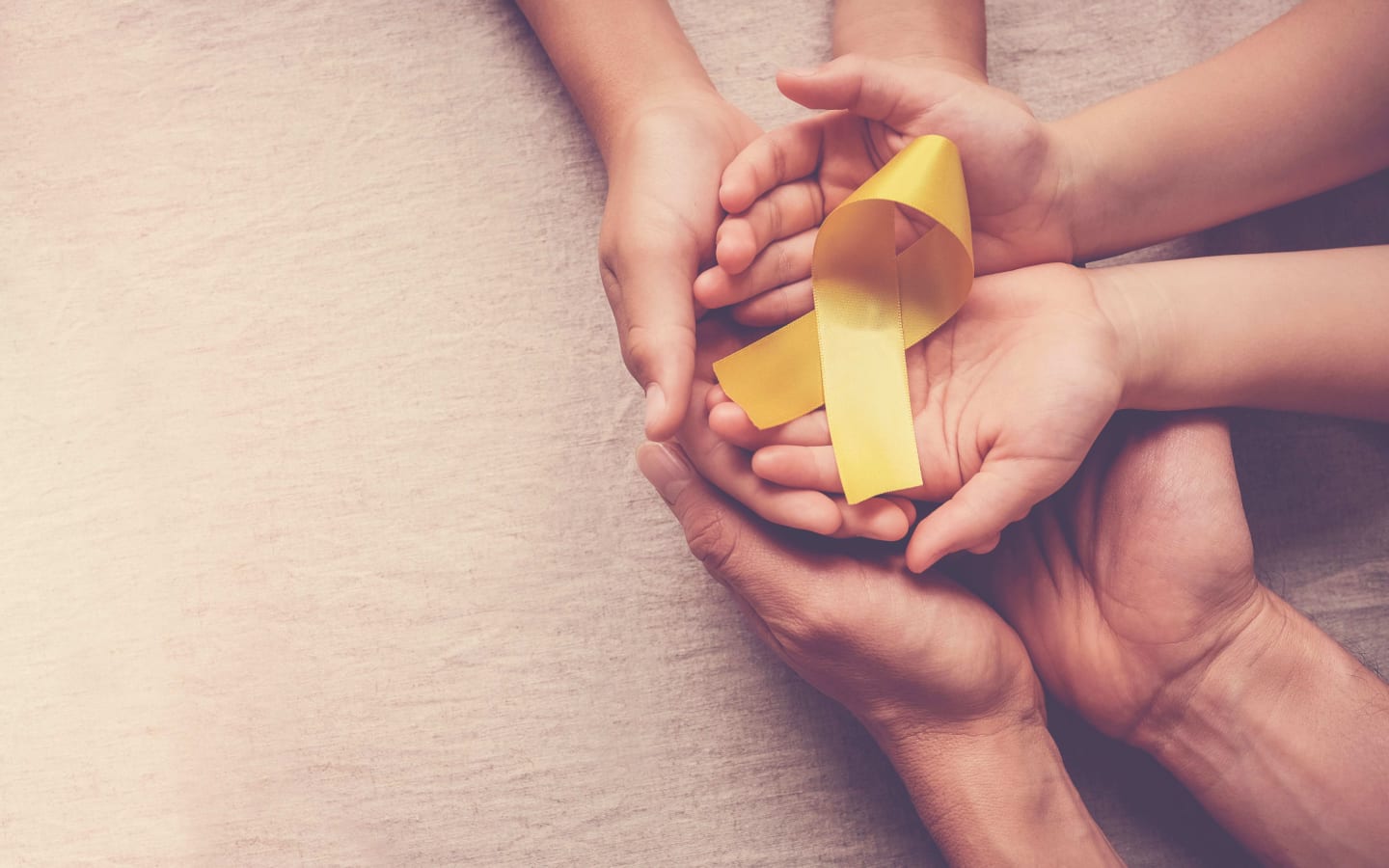 Three sets of hands holding a yellow ribbon symbolizing cancer