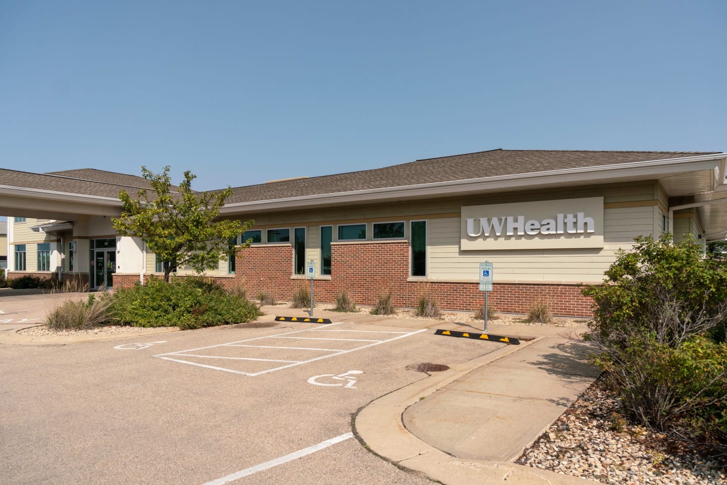 A single story building with cream-colored siding and red brick with a white UW Health sign