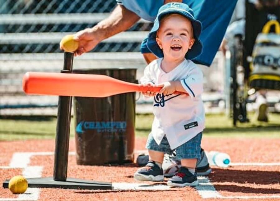 Toddler Colton Cox, swinging a plactic baseball bat at a tee, wearing a Kansas City Royals jersey and hat