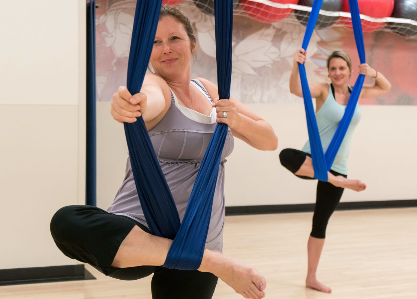 Two women in tights stetching their legs with a suspended rope