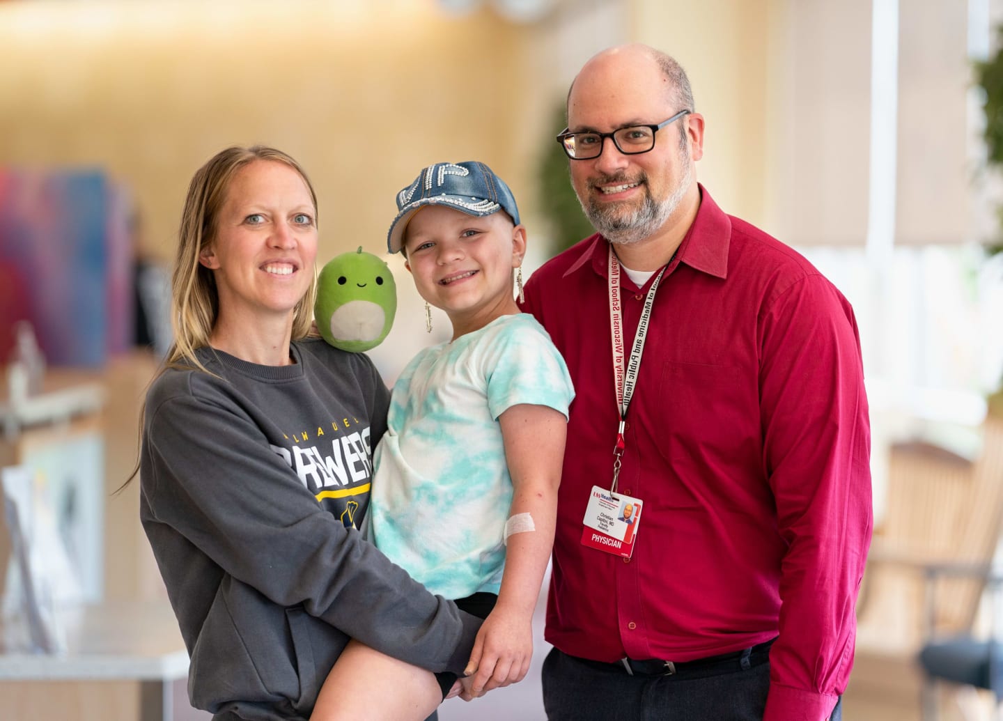 Portrait of Dr. Christian Capitini in a red shirt with patient Scarlett being held by her mom