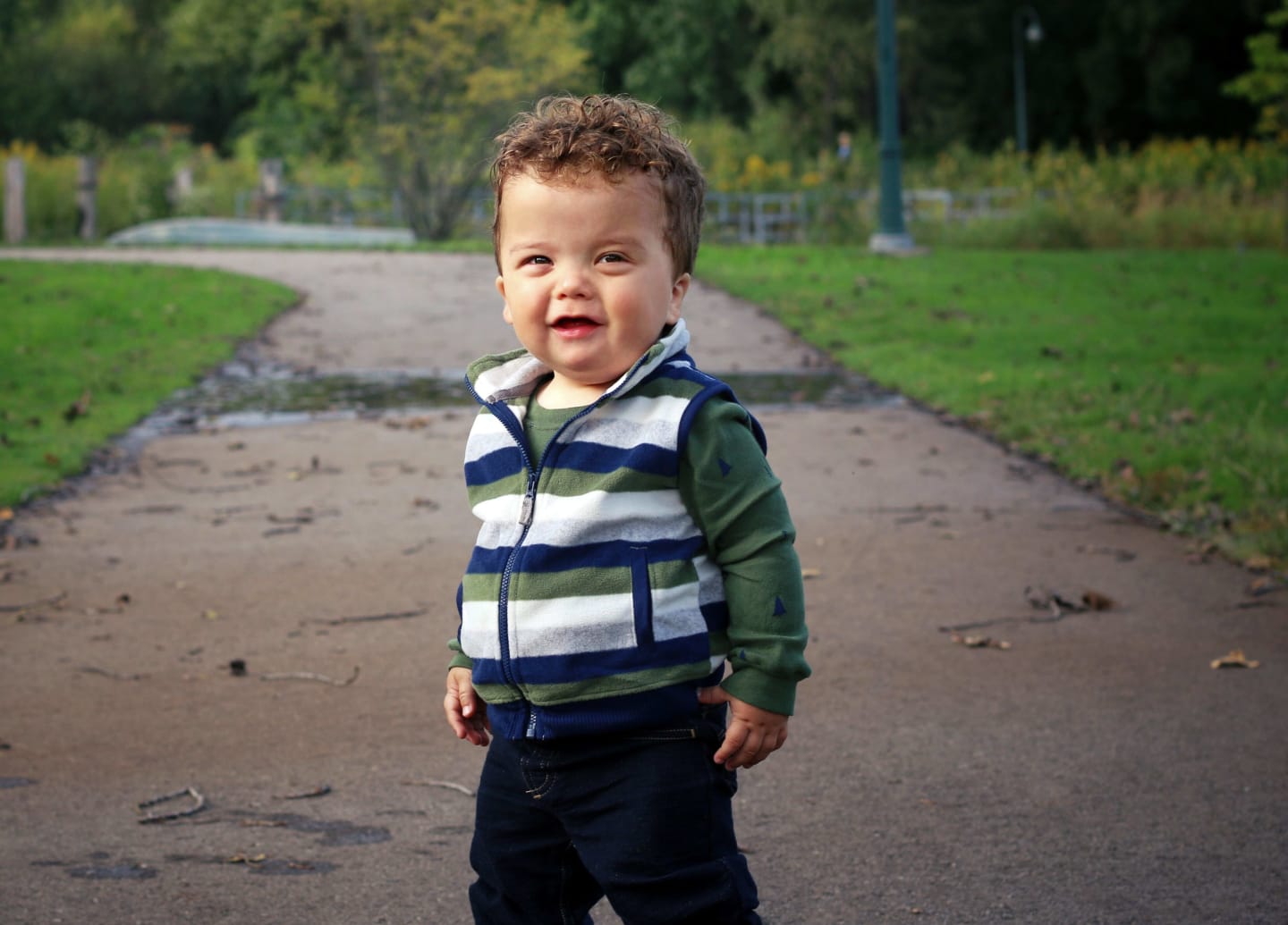 Toddler Titus standing on a paved path in a park