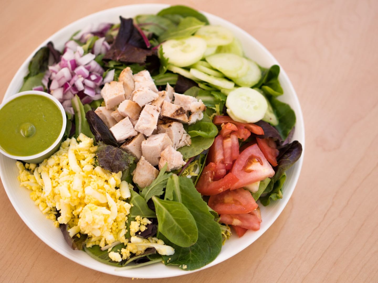 Salad with eggs, turkey, cucumbers, onions and a green vinaigrette dressing in a white bowl