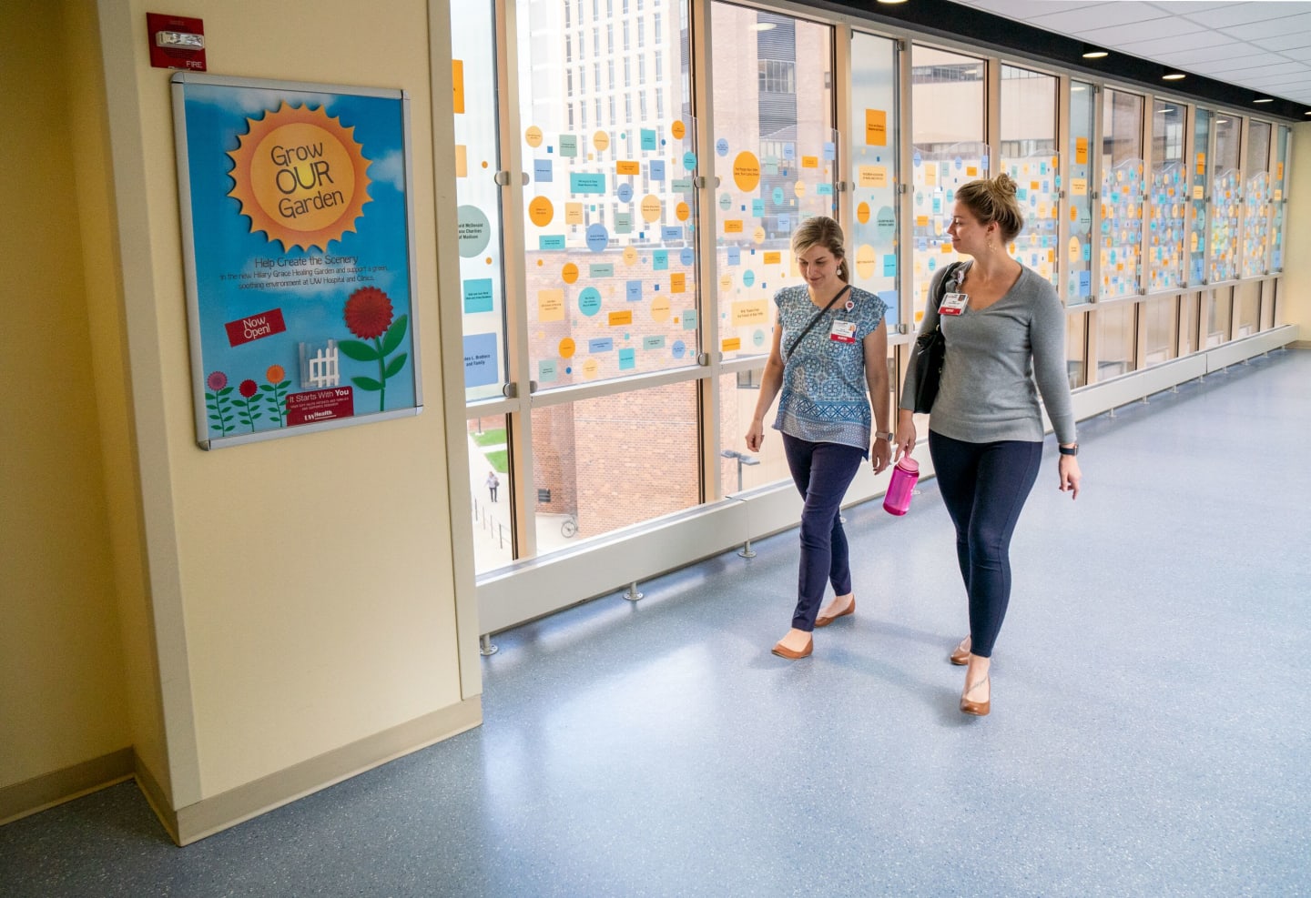 Two UW Health employees walking through a hallway of windows