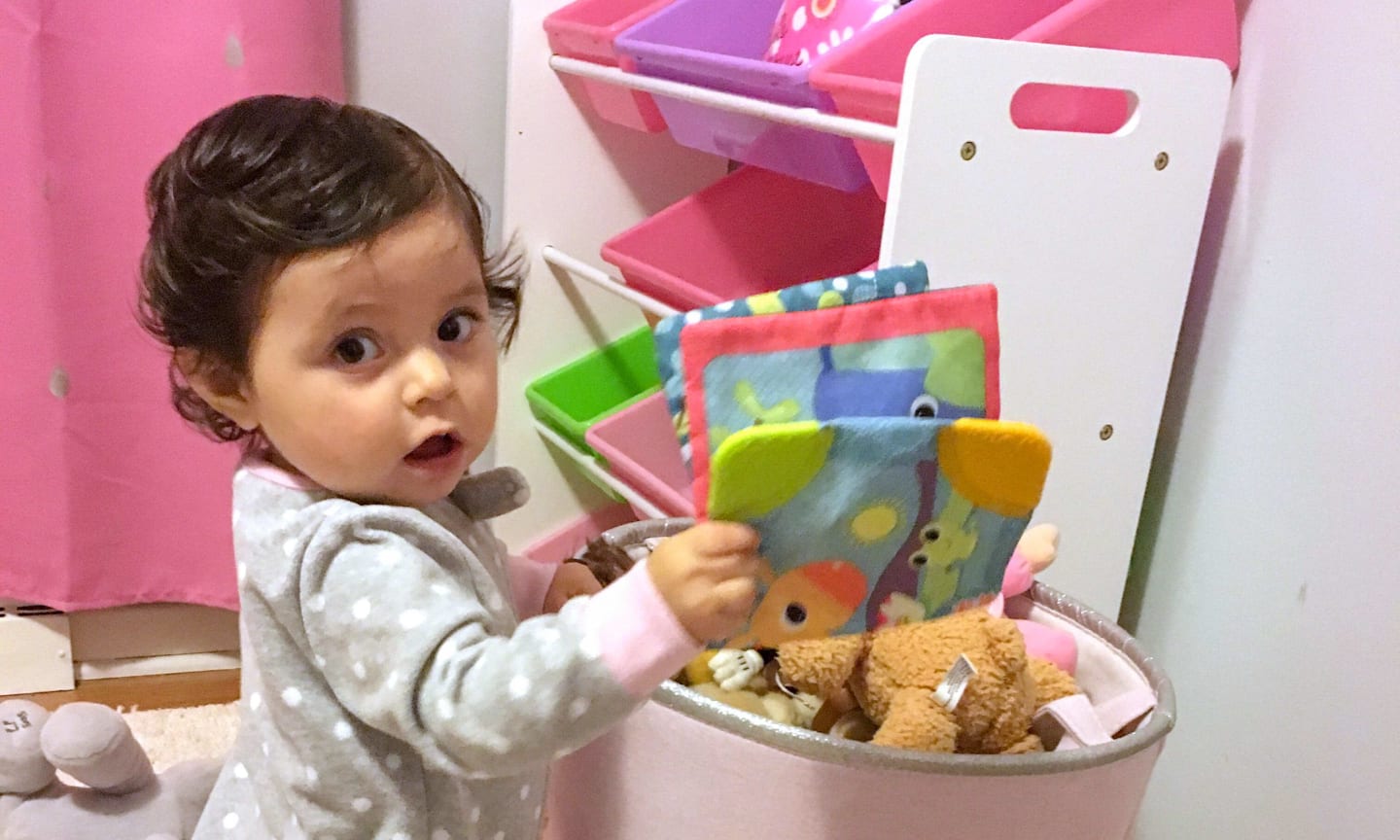 Milena Leon, a baby, standing in front of a basket of toys