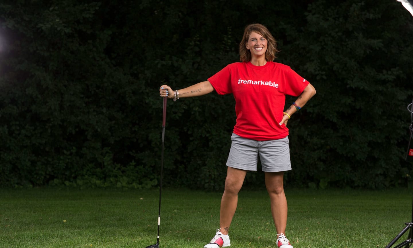 A woman holding a golf club, wearing a t-shirt that reads "remarkable"