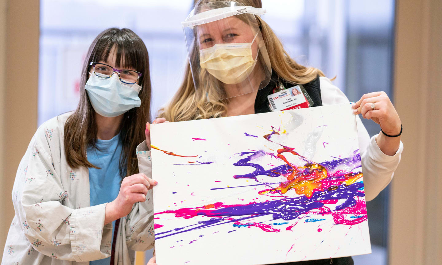 Two medical providers, wearing surgical masks, holding children's art work