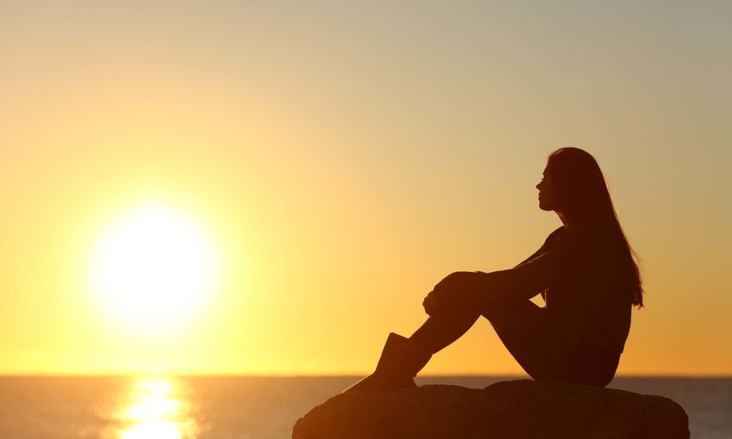 A silhouette of a person watching a sunset over a large body of water