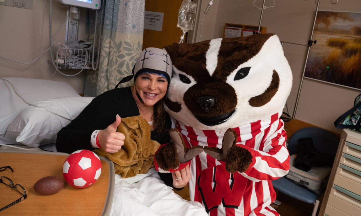 A patient wearing a cooling cap being visted by University of Wisconsin mascot Bucky Badger