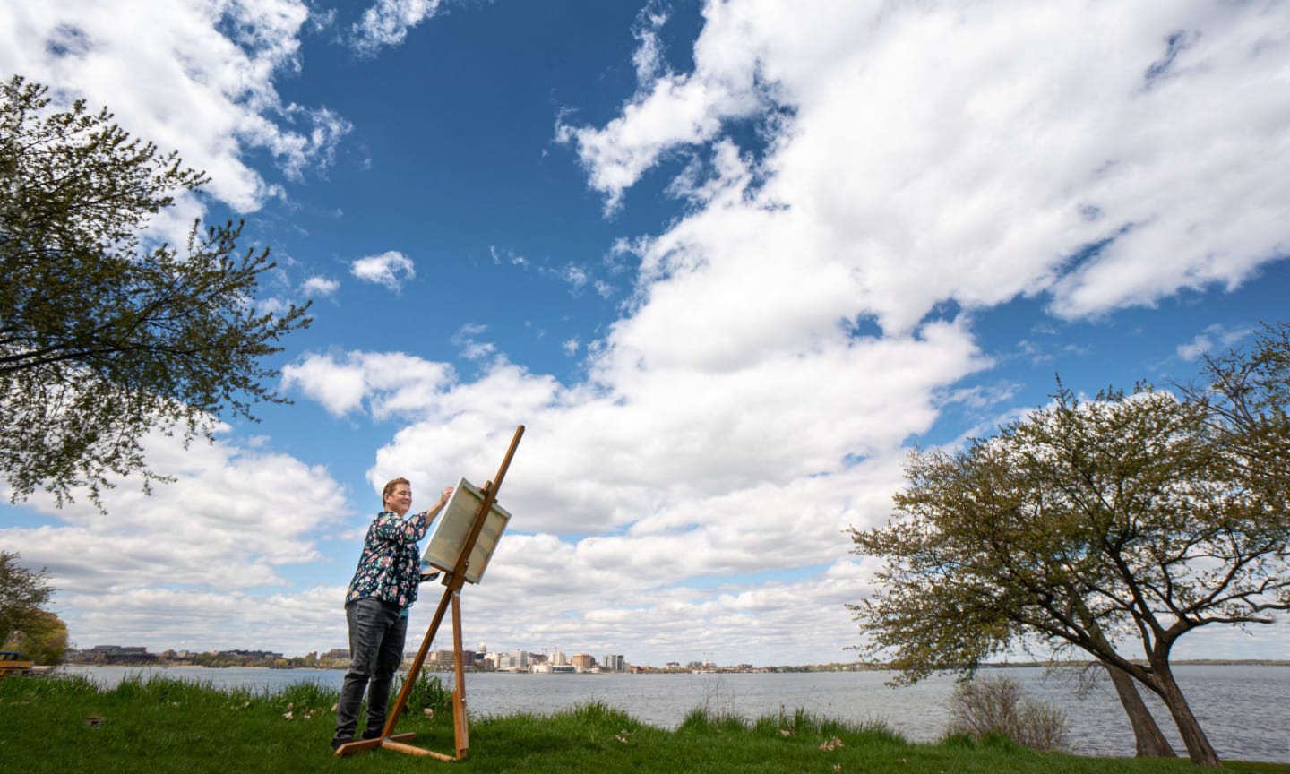 Lorry Adkins painting on an easel next to a lake