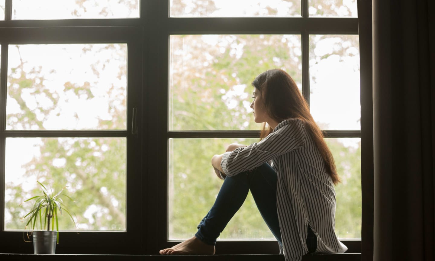 A person sitting in a window sill, looking outside