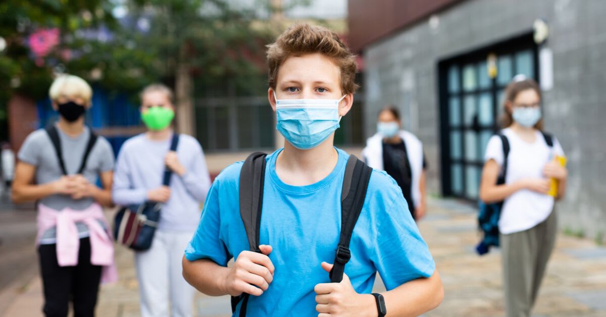 Teenagers wearing medical masks and backpacks in a school yard