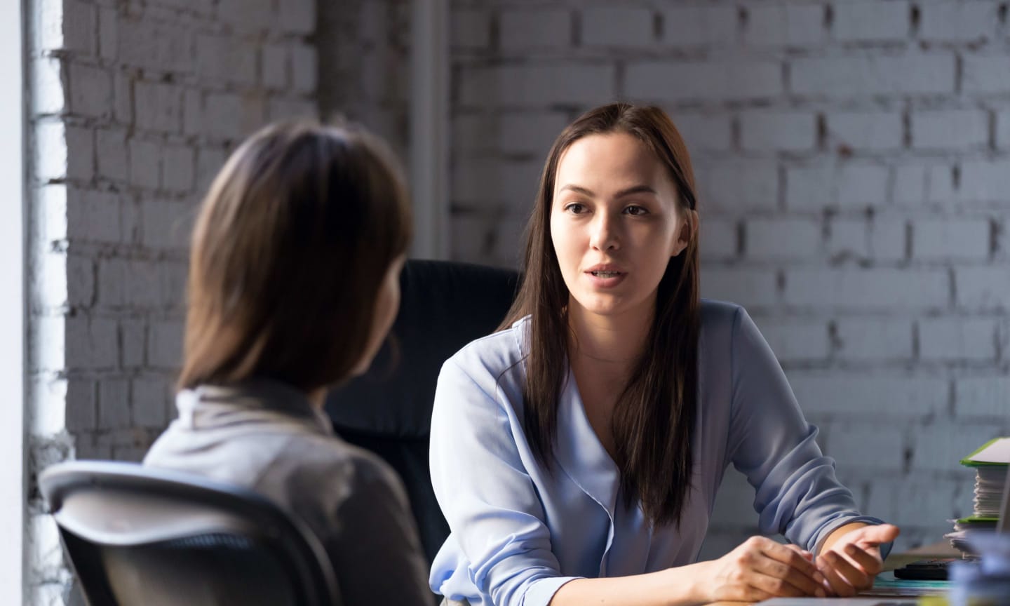 Two individuals talking at a desk