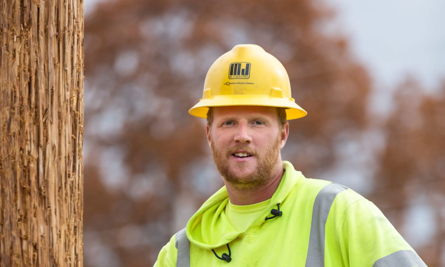 Landen Wilke, wearing high visibility clothing, climbing an electrical pole