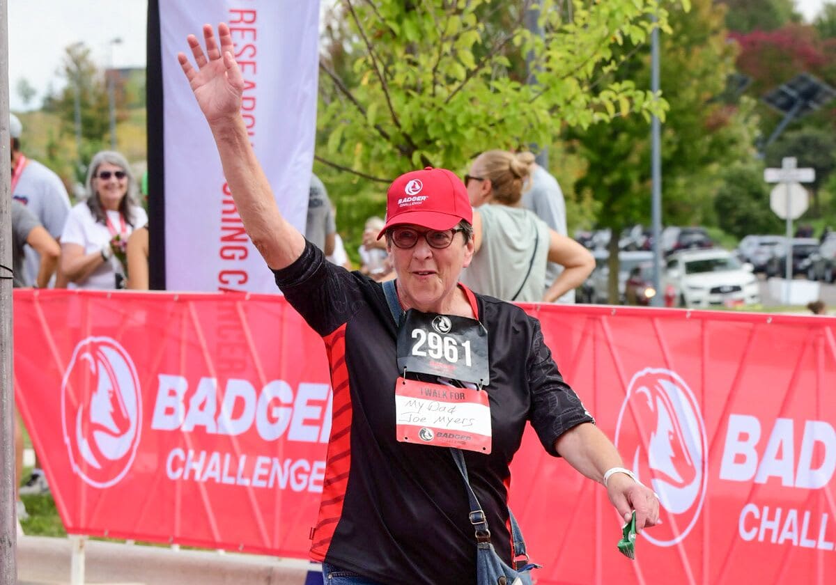 Mary Kay Schimming waving while crossing a finish line at a run-walk event