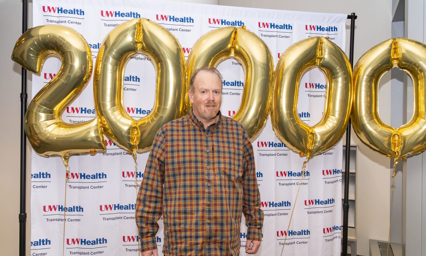 Man in a plaid shirt standing in front of balloons spelling twenty-thousand