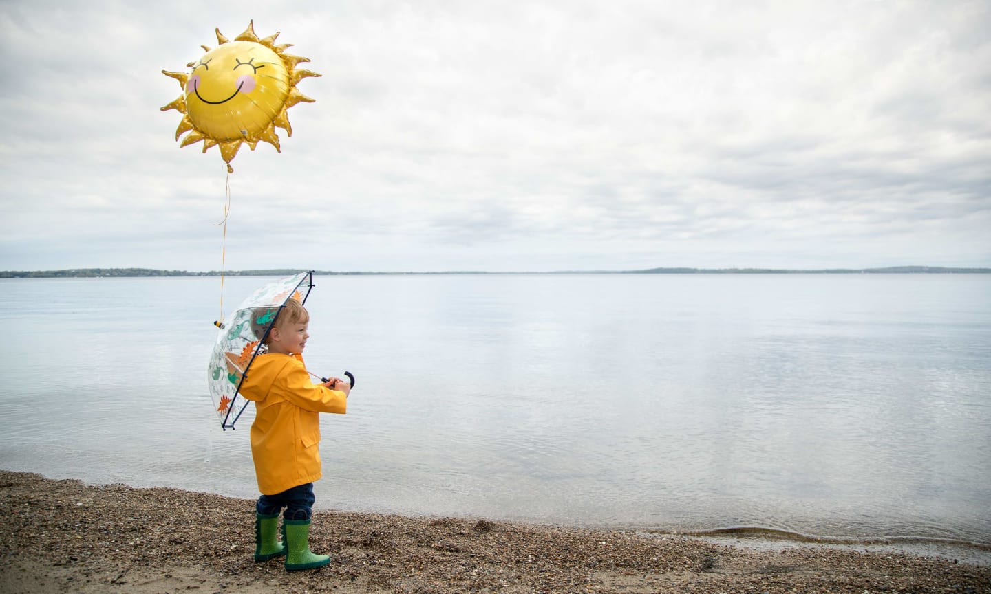 Rykal Wasson standing on the shore of a lake, wearing rain coat, holding a balloon
