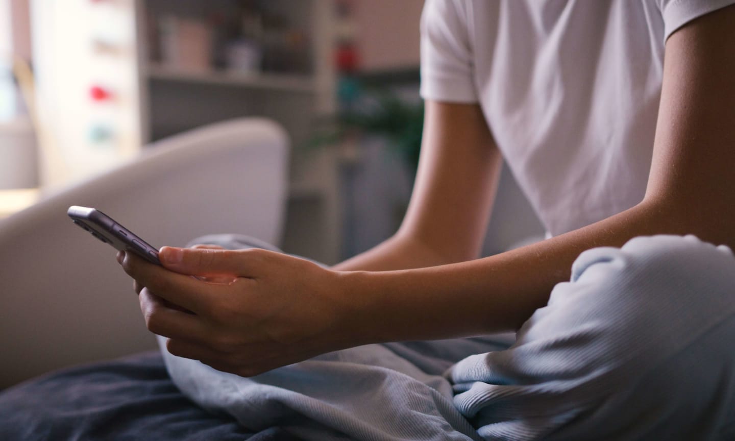 Close Up Of Teenage Girl Sitting On Bed At Home Looking At Mobile Phone