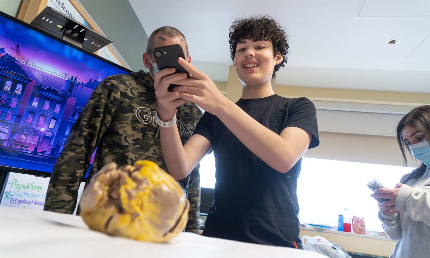 A teenage boy takes a photo with his phone of the heart he was born with
