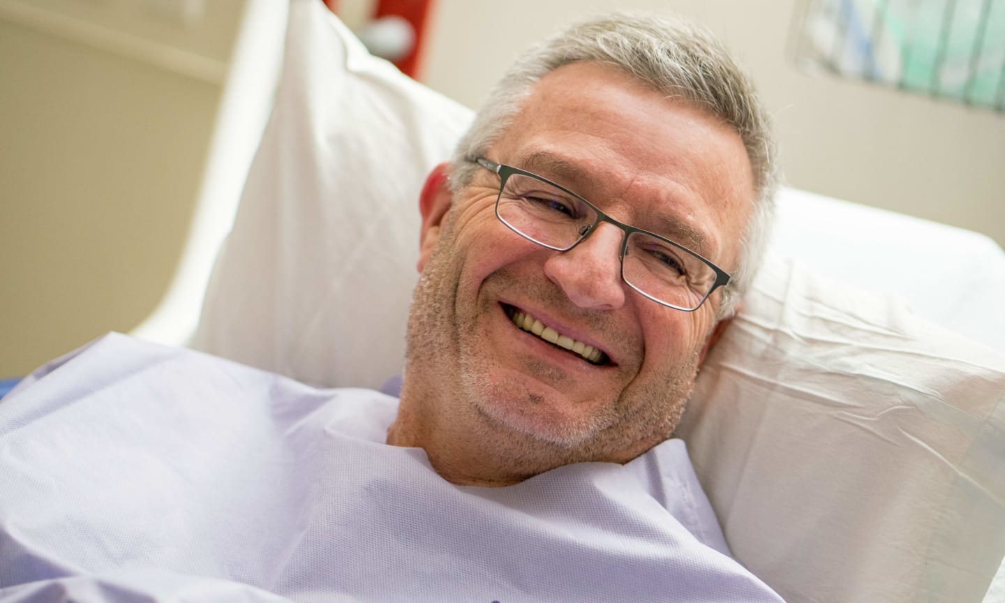 Jay Wilson, smiling, propped up against a pillow in a hospital bed