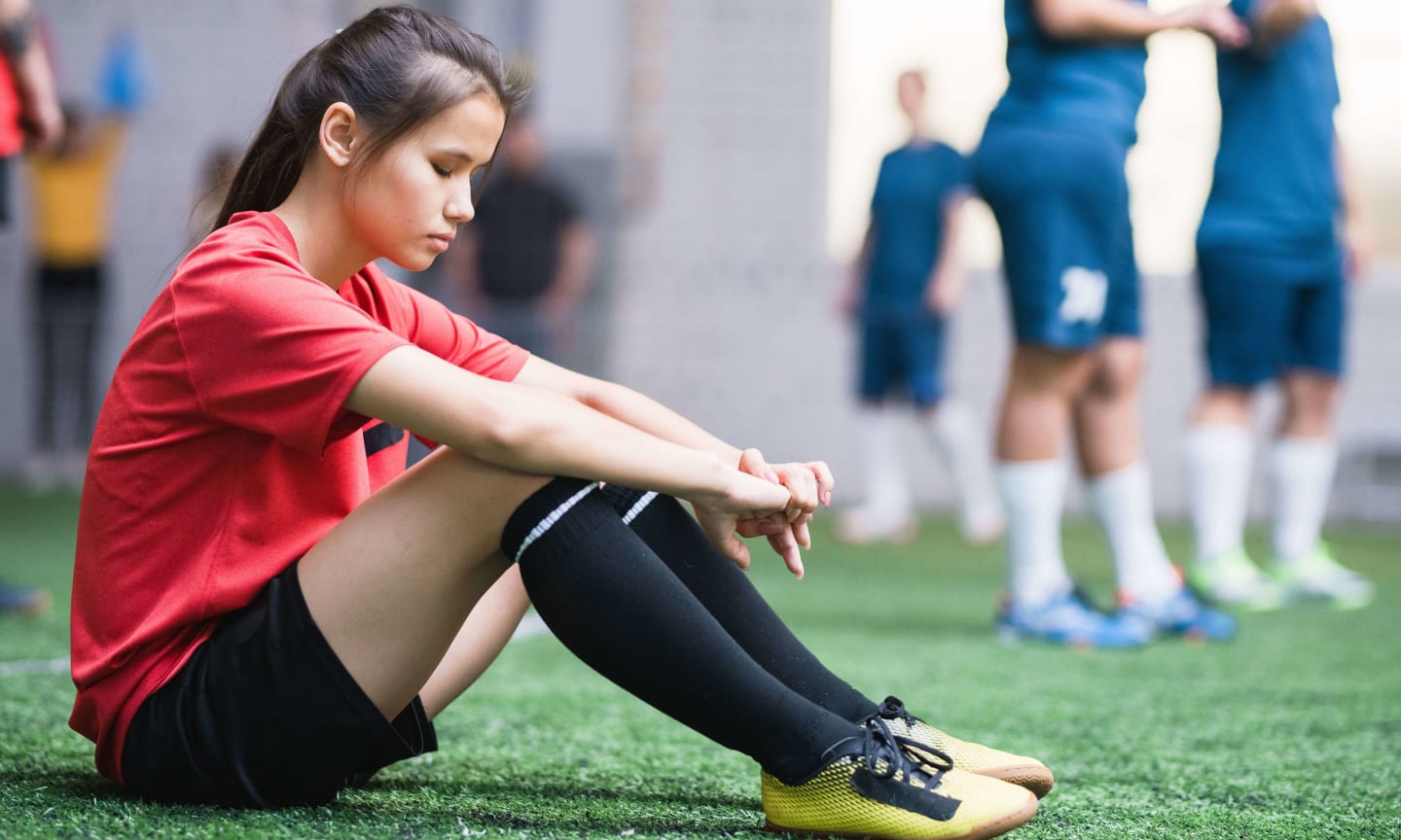 A soccer player sitting on the ground with a sad expression on their face