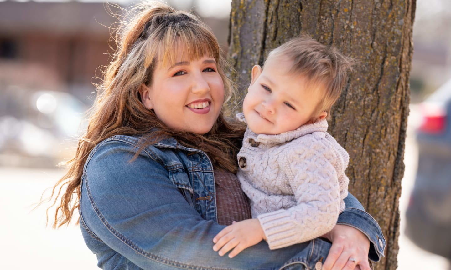 Kym Pfister holding her 2-year-old-son, Gus, in front of a tree trunk