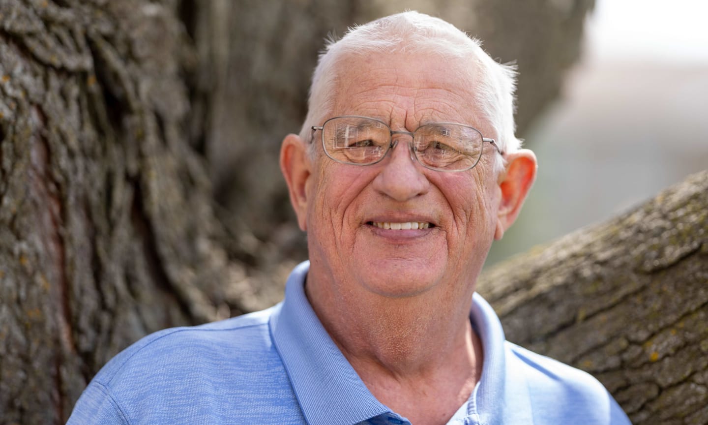 Man smiling outdoors in front of a tree.