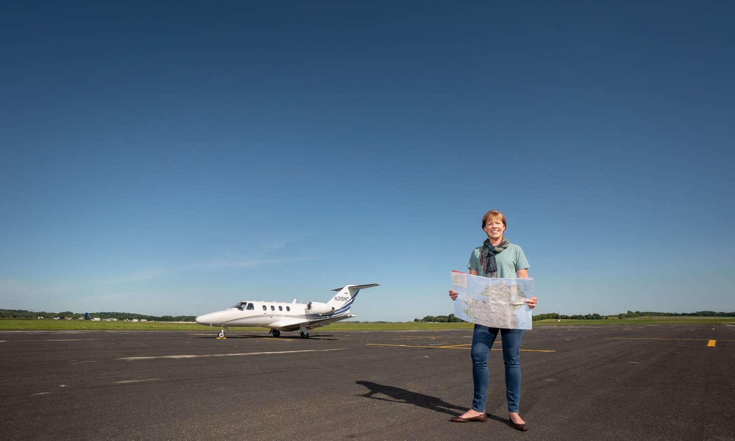 Marie Ganser standing in front of a small airplane, holding a map