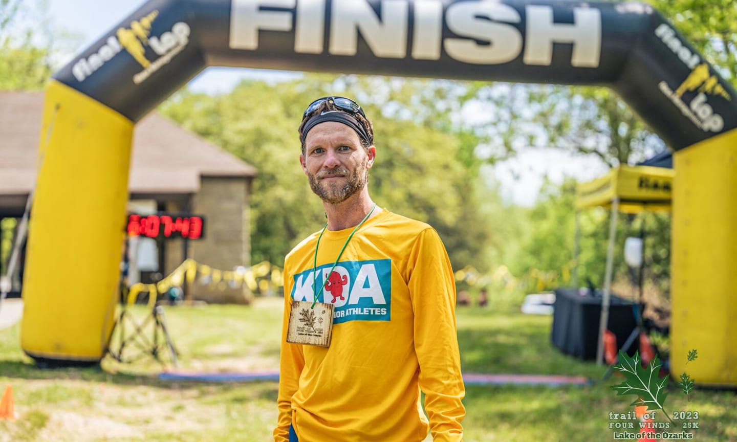 Man in running gear standing in front of a finish line at a race.