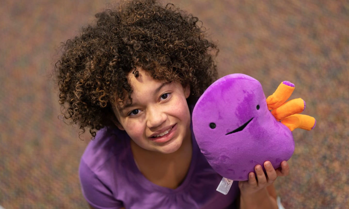 Lyla Cola smiling and holding a stuffed plush kidney toy.