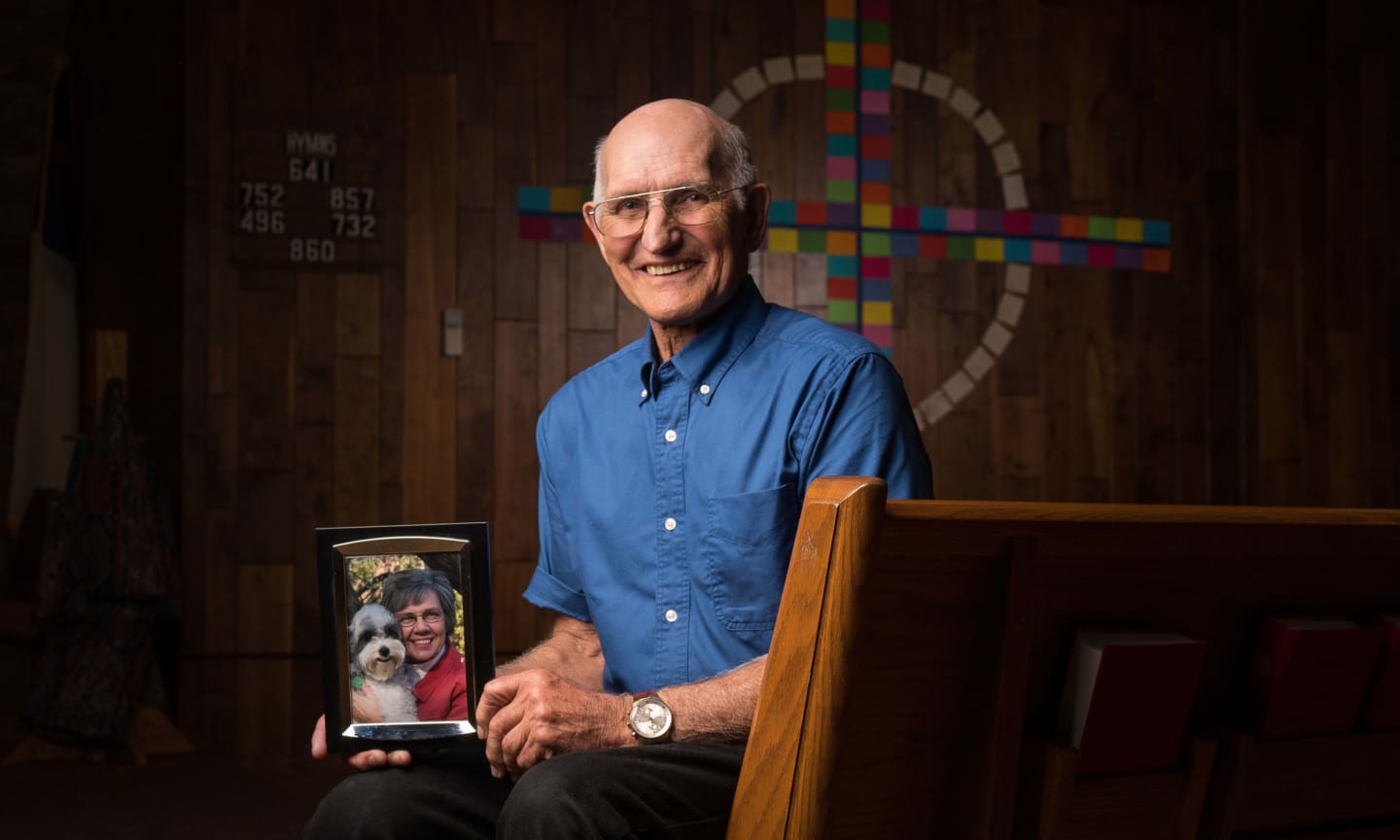 Al Wright, sitting in a church pew, holding a photo of his wife Charlene