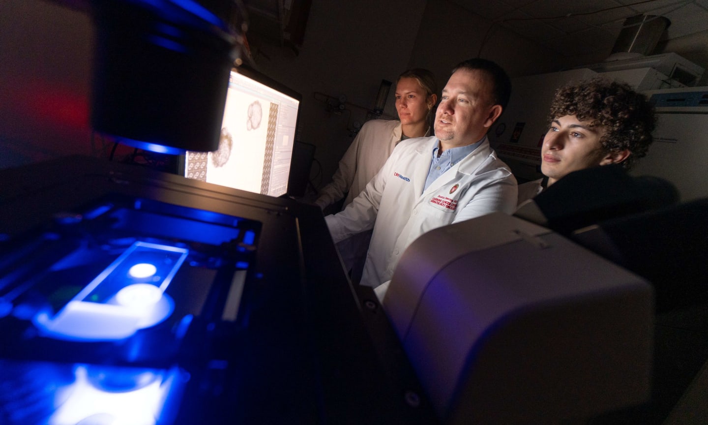 Three medical researchers reviewing imaging in a darkened laboratory