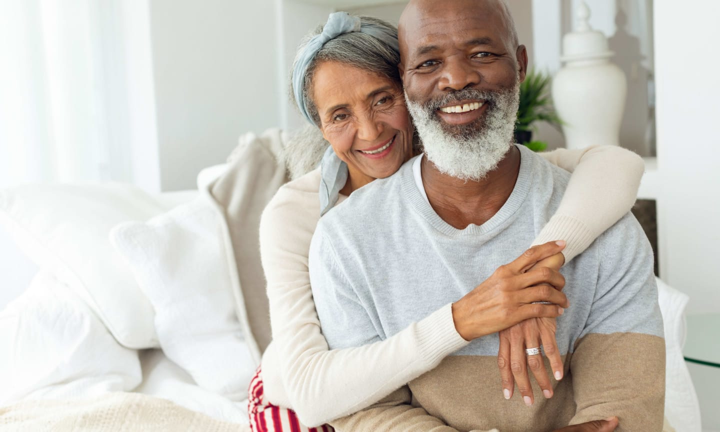 Front view of happy senior diverse couple sitting in a white room in beach house. Authentic Senior Retired Life Concept