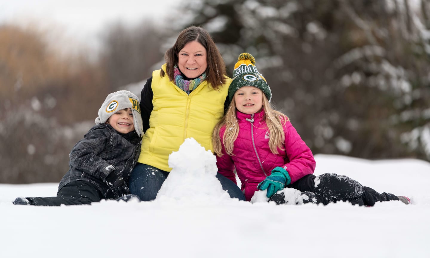 Kate Erd playing in the snow with her two grandchildren, who are both wearing Green Bay Packers knit hats