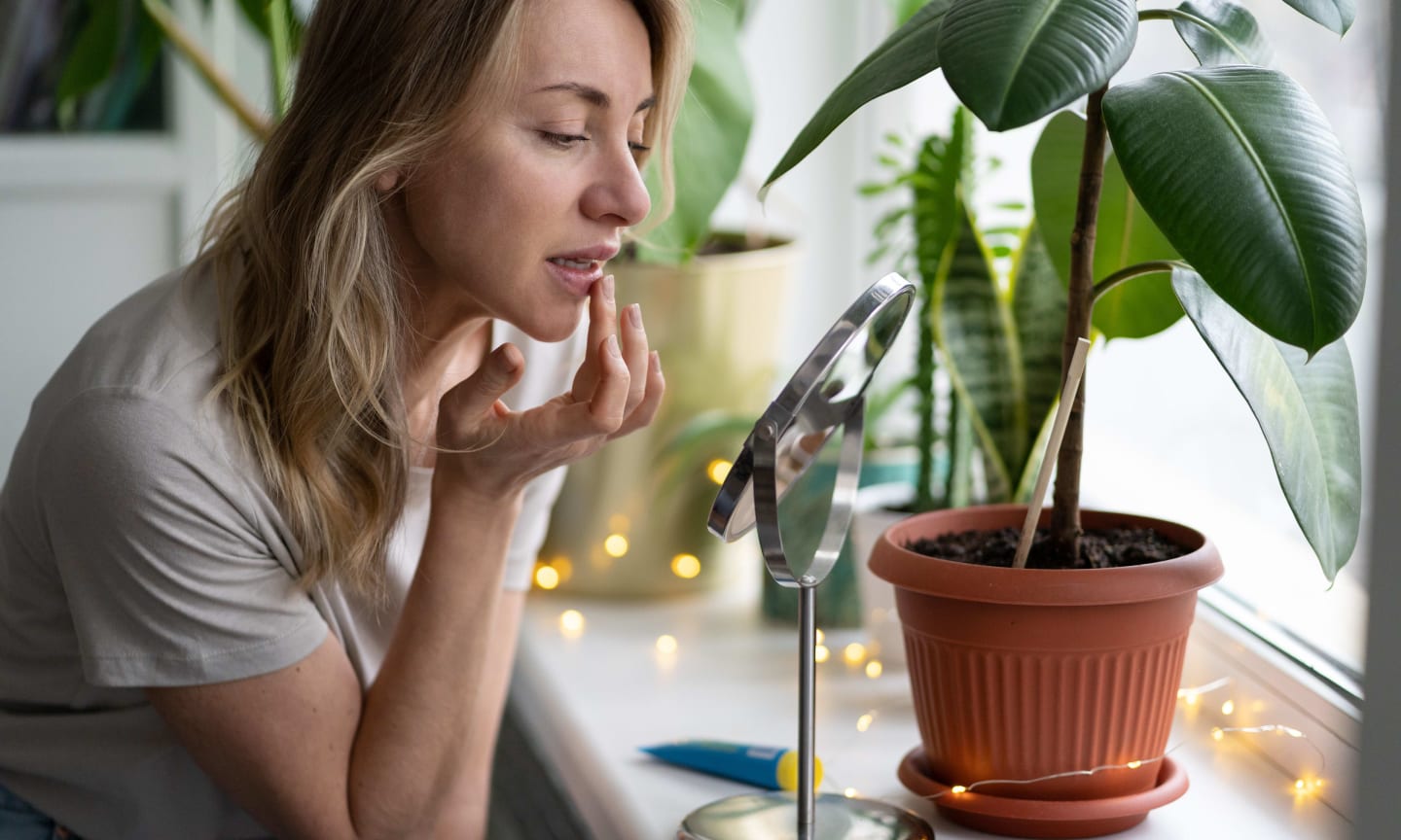 A woman applying lip balm in front of a mirror and house plants