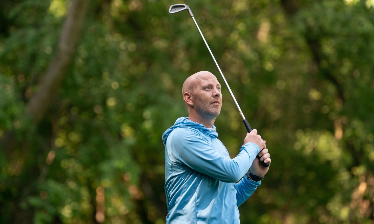 Patrick Leigh outdoors swinging a golf club and wearing a blue long sleeve hoodie.