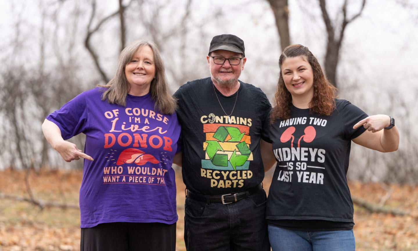 The two women standing on either side of a man, smiling. The woman on the left donated her liver, and on the right donated her kidney.