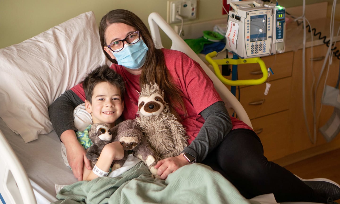 Christian Pribbernow receiving a hug from his mother, Kellie, in a hospital bed with a sloth stuffed animal